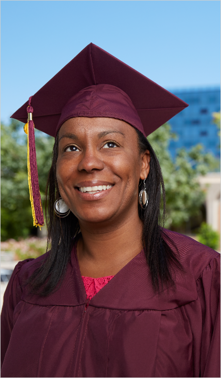 An ASU graduate poses on the Tempe campus wearing graduation regalia.