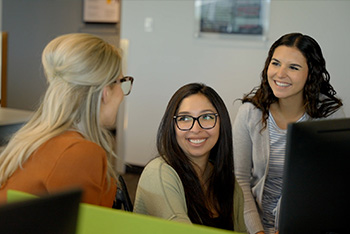 Three women smiling and talking in an office setting.